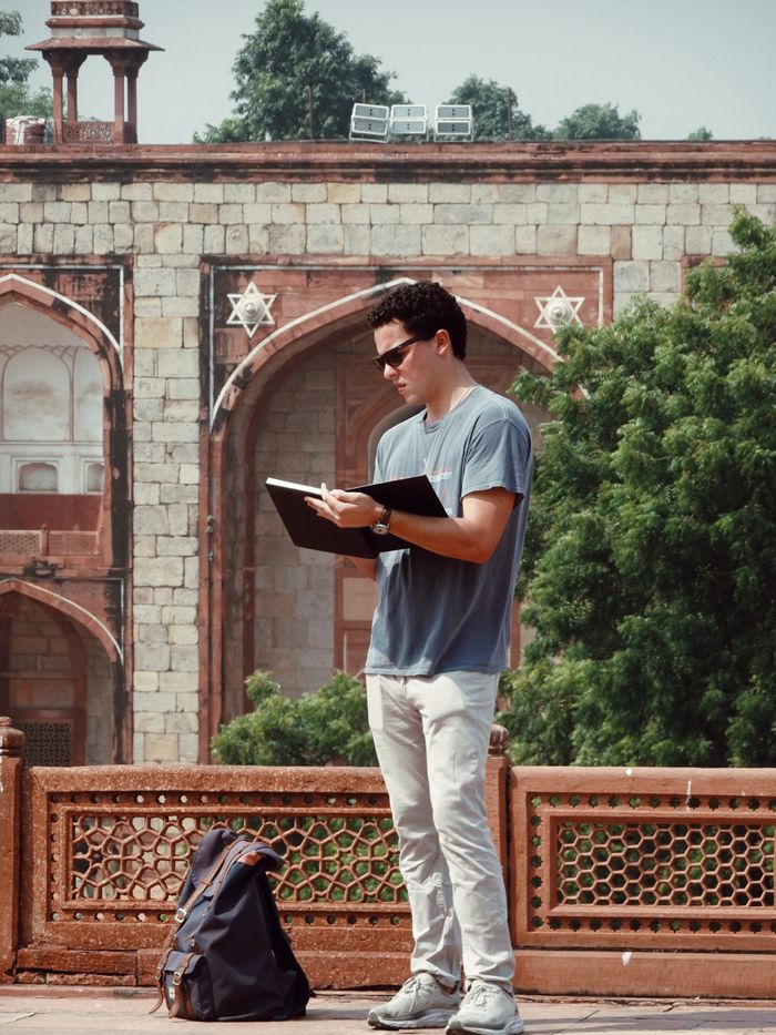 Man with sunglasses writing in journal at historical landmark outdoors.