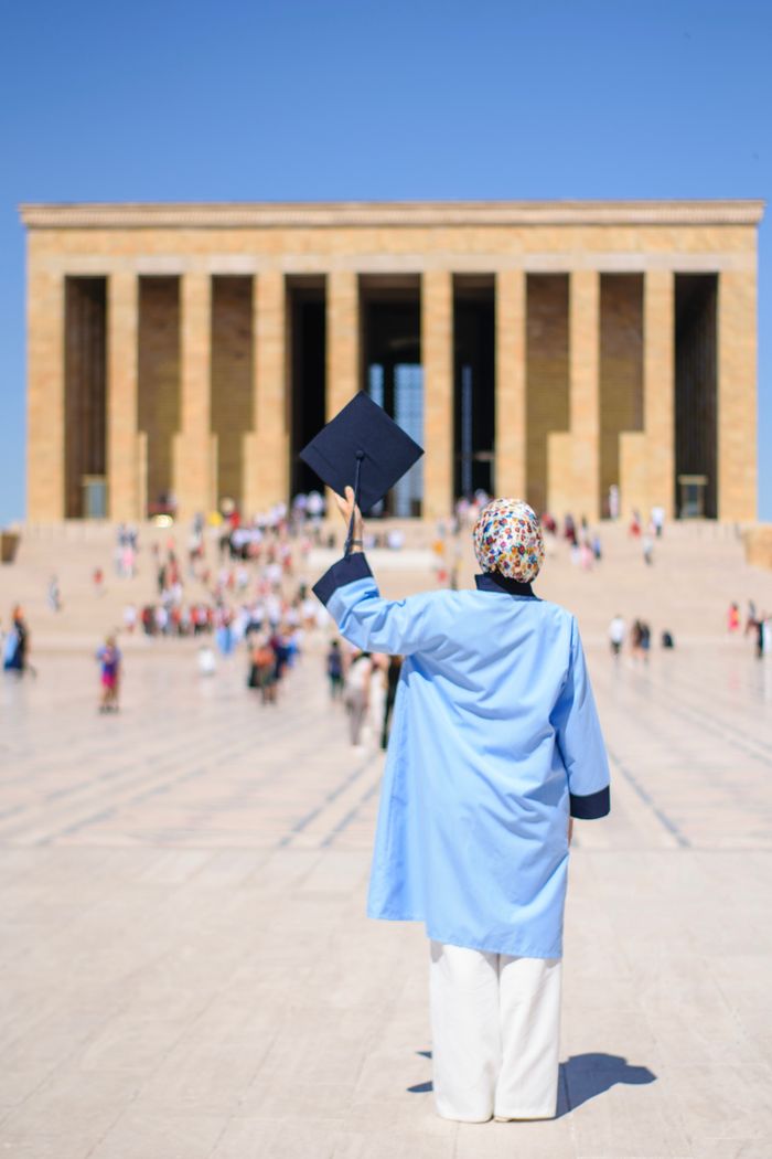 A graduate celebrates at Anıtkabir in Ankara, Turkey, holding a mortarboard.
