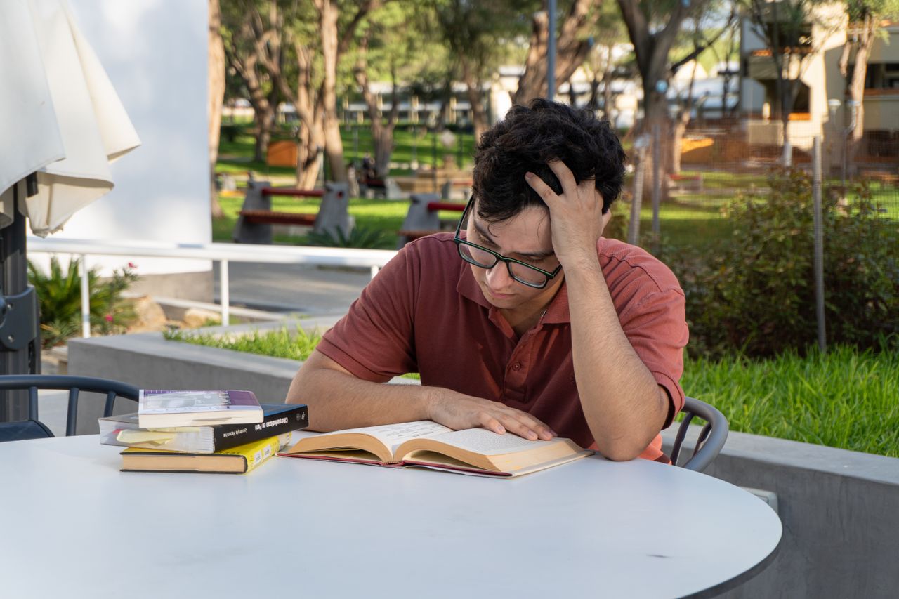 A young man focused on studying books outdoors at a university campus in Piura, Peru.